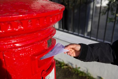 A close up image showing a child's hand posting a letter into a red postbox