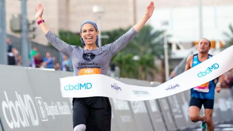 Beatie Deutsch crossing the finish line of the Tel Aviv marathon, her arms raised in the air