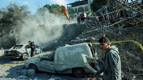 young men are seen near damaged cars at the site of an Israeli air strike near Byblos