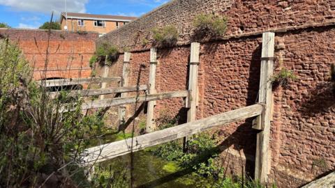 Albert Street Cutting in Bridgwater. There are only wooden boards left, which are connected to a red brick wall by the canal.