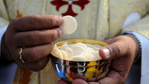 Priest holds a cup of wafers