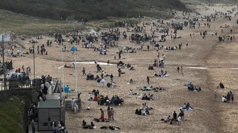 Long Sands beach during the bank holiday weekend of 2 May, 2026. Swarms of people can be seen stretching across the coastline, even though it did not appear to be particularly sunny when this photo was taken. In one corner, a group can be seen climbing on top of a cabin roof.