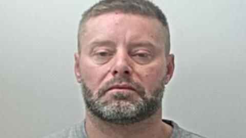 Kevin Thompson's mugshot. He has short grey hair and a short salt and pepper beard
