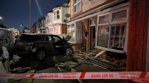 A badly damaged Range Rover in rubble next to a damaged house