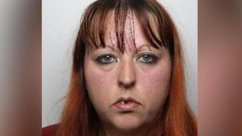 A mugshot of Stubbs, who has long, straight hair that transitions from a darker shade at the roots to a reddish-brown or auburn colour toward the ends. The hair falls over the shoulders.