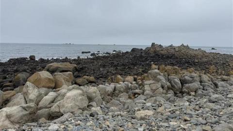 Portinfer rock pools. A landscape image of the rocks and the sea in the background. The sky is overcast. 