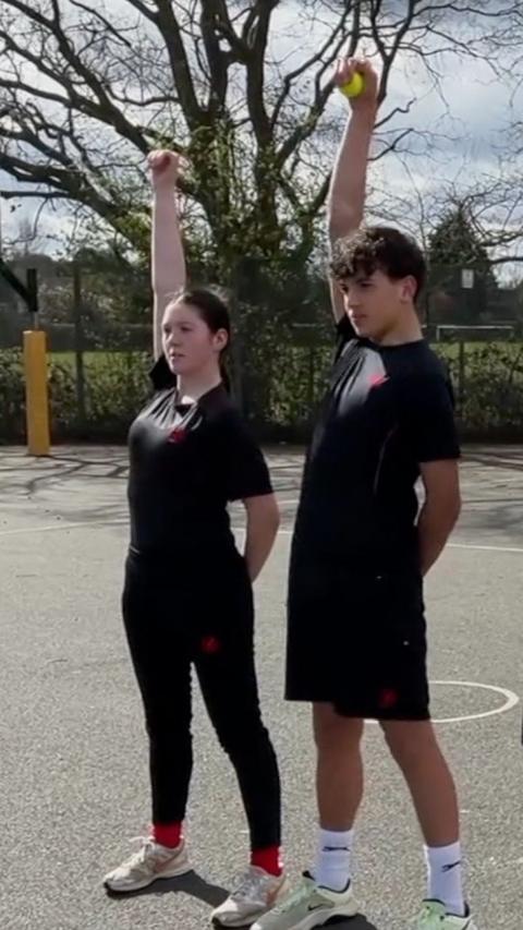 A young girl and a young boy both holding tennis balls above their heads