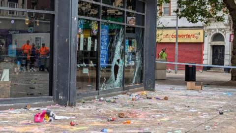 Hull's Lush store behind police tape after it was the scene of looting. Broken windows can be seen and the pavement outside the shop is covered in the remnants of colourful bath products.