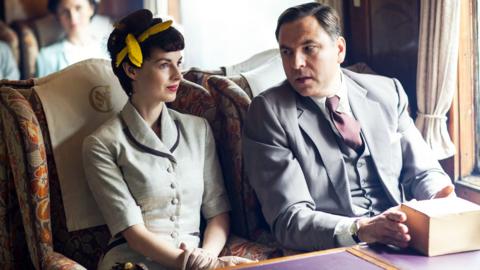 Jessica Raine and David Walliams, as Tuppence and Tommy Beresford in Partners in Crime. The couple sit next to each other on a old-fashioned train.