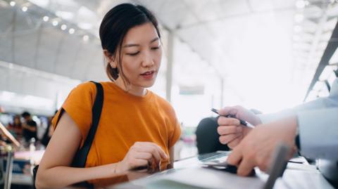 Young woman wearing an orange T-shirt checking in at an airline check-in counter at an airport