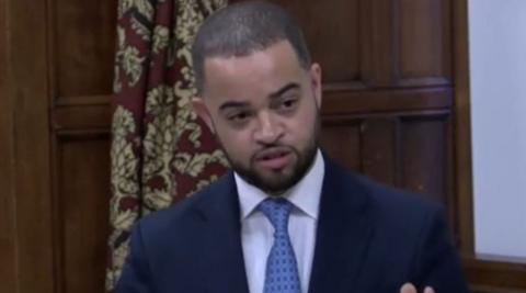 Newcastle-under-Lyme MP Adam Jogee wearing a dark jacket, white shirt and light blue kit. He is standing up during a Westminster Hall debate.