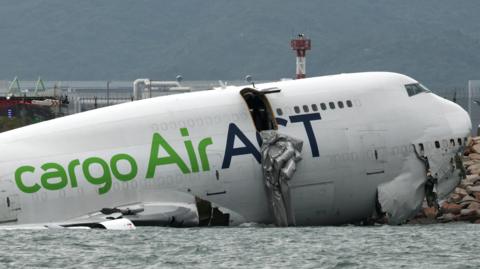 A cargo plane lies partially in the sea after veering off the runway during landing at Hong Kong