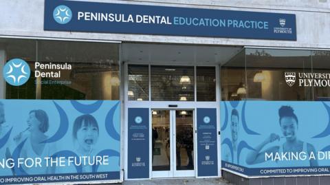 The front of the shop with a blue front with the Peninsula Dental and University of Plymouth signs