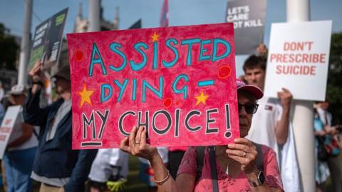 People protest in support of the assisted dying bill at Westminster. A woman is holding a large pink banner saying "assisted dying - my choice" is at the front of the picture.