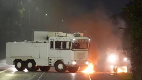 A white water cannon vehicle next to a fire on the road