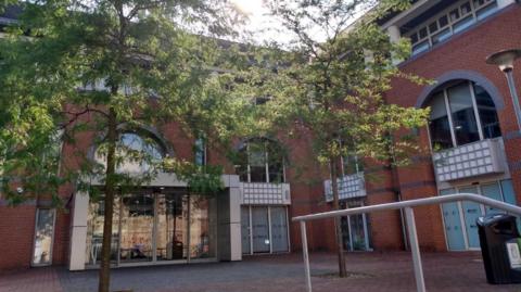 Reading Borough Council offices, photo taken from the street of a red brick buildings with 4 arch windows and doors for various entrances and two tall trees with green leaves in the forecourt