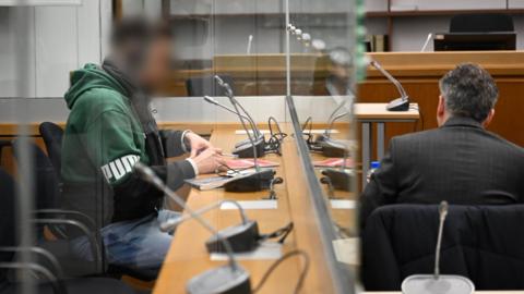 The defendant, a suspected member of Hezbollah, sits behind a glass wall before the start of his trial at the Higher Regional Court in Celle.