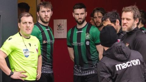 Match officials and Aberystwyth players wait for news at the USW Sport Park in Treforst