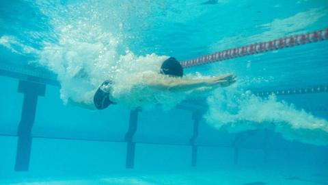 A man underwater in a swimming pool with his arms outstretched in front of him, as if he has just dived into the pool. 