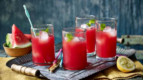 Four glasses of watermelon coolers filled with ice and topped with mint.