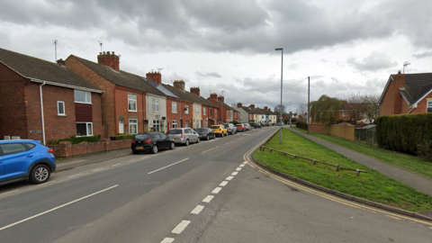 A general view of a street of houses with cars parked along the left-hand side of the road