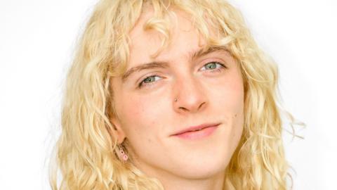 A close-up photograph of Alexa Moore looking to camera.  She has long, waving blonde hair and is wearing a nose stud and a pink earring.