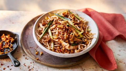 A bowl of Peanut chilli crisp noodles with chicken and cucumber next to a red cloth