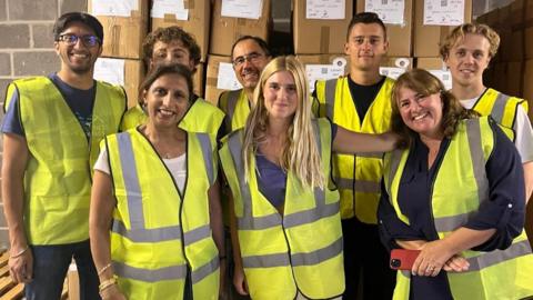 Eight people standing in front of boxes ready to be sent to Lebanon