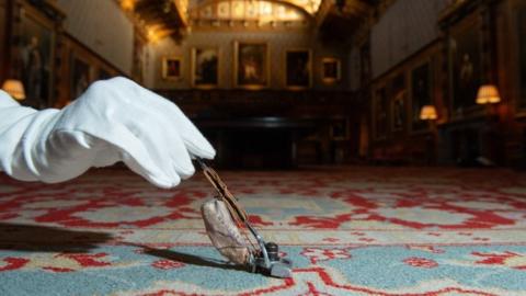 A gloved hand holds a miniature hoover in one of the rooms of Queen Mary's dolls' house