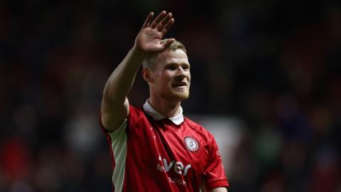 Bristol City defender Rob Atkinson, wearing red and white home kit, holds his hand up in the air