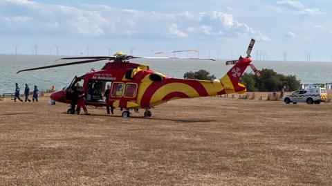 A red and yellow air ambulance on Frinton-on-Sea's Greensward - a large, open area of grass by the seafront.