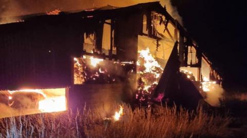 A large barn engulfed in flames burning against the night sky