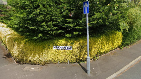 A street view of a close with a green bush and a road sign reading 'KIRKHAM AVE'.