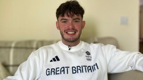 Ed Lowe sitting on a sofa wearing his Great Britain jumper, proudly looking at the camera