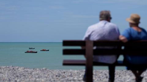 A couple watch two small boats hug the coastline near Ault in France as people thought to be migrants attempt to cross the Channel in June