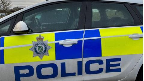 A side view of a Lincolnshire Police patrol car with blue and yellow markings and the force's badge on the door 