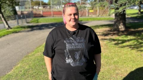 Lorraine Parbury standing at a park wearing a black Liverpool top with coloured pink hair