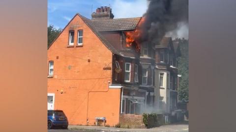 A Victorian home with flames coming out of the top-floor window.