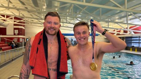 Olympic swimmer Adam Peaty OBE standing next to BBC Radio Derby's sports presenter Dominic Dietrich at a pool in Uttoxeter.