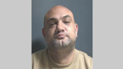 Ashley McNeil has his head tilted upwards and is looking directly at the camera. He is wearing a beige jumper and has stubble across his chin. 