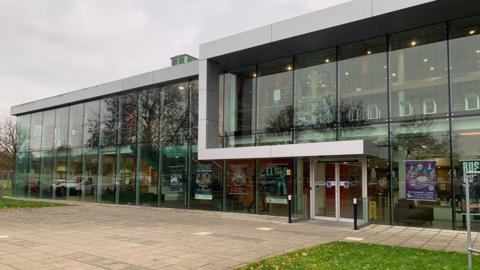 Exterior of the Key Theatre- a glass window with grass in front of it 