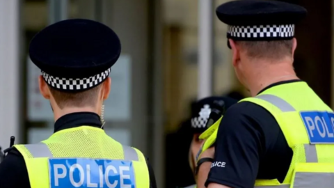 The back of two police officers dressed in uniform, including police hats and vests with 'POLICE' written on the back