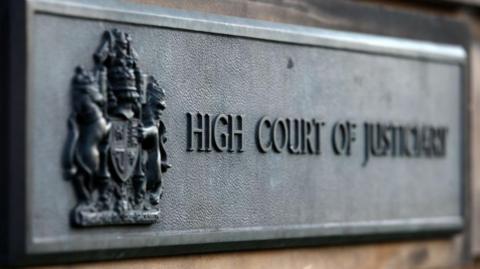 Grey court sign with words 'High Court of Justiciary' in block capitals at the High Court in Edinburgh