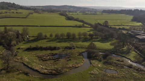 A landscape of fields and trees with a winding river in the foreground