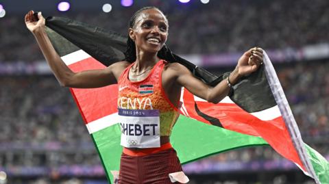 Beatrice Chebet celebrates with a Kenyan flag after winning the women's 10,000m at Paris 2024