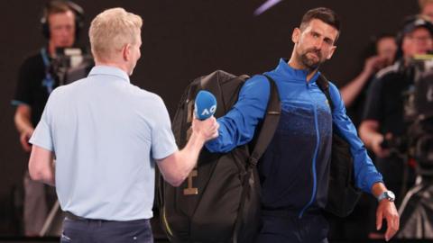 Novak Djokovic hands back the microphone to the on-court interviewer at the Australian Open.