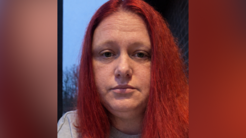 A selfie style image of a woman with long red hair. She is looking emotionlessly into the camera.