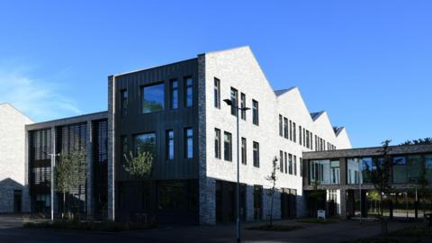 A modern school building, coloured grey, on a bright, sunny day