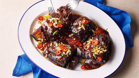 A bowl of braised beef short ribs, topped with green onions, nuts and slices of chilli.