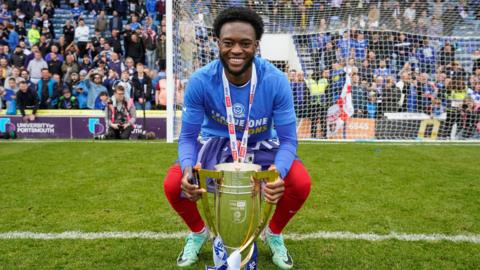 Abu Kamara poses for a photo with the League One trophy after the club completed their final game of the season